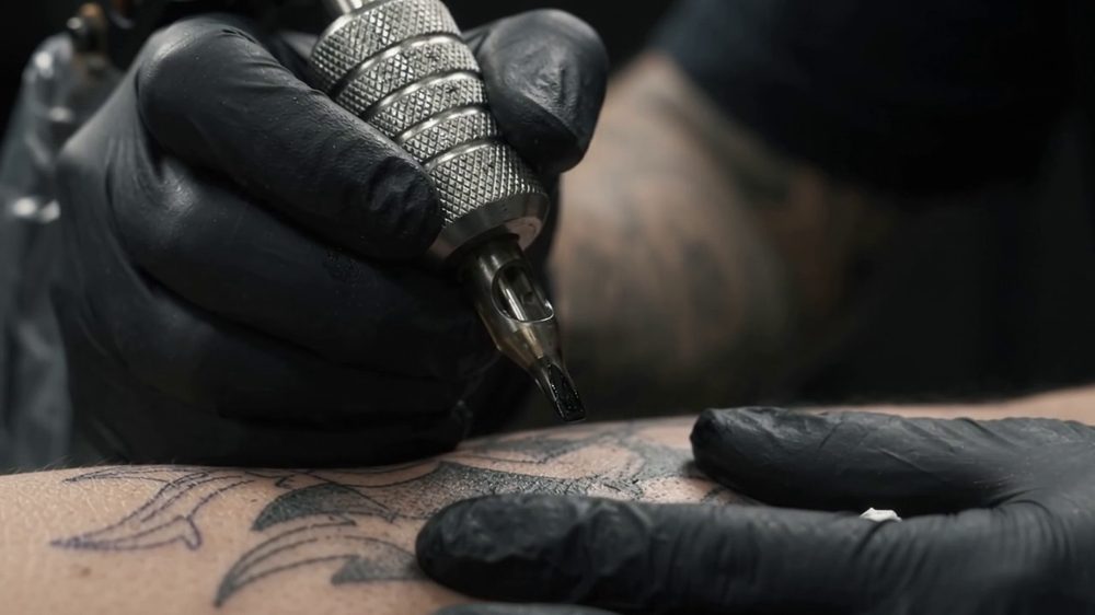 Mãos com luvas pretas a tatuar o contorno de um desenho