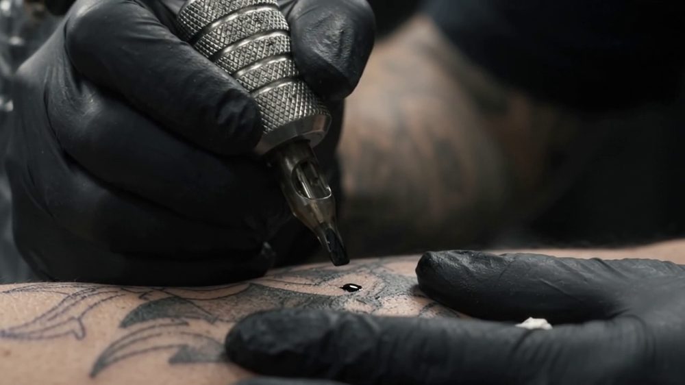 Máquina de tatuar em grande plano a contornar um desenho na pele